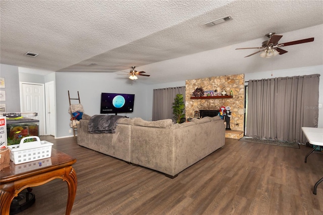 living room featuring a textured ceiling, a stone fireplace, ceiling fan, and dark hardwood / wood-style floors