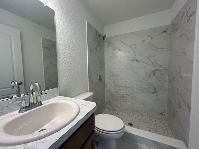 bathroom with tiled shower, vanity, and toilet