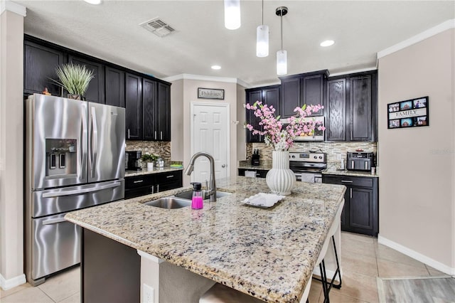 kitchen with stainless steel appliances, hanging light fixtures, sink, an island with sink, and backsplash