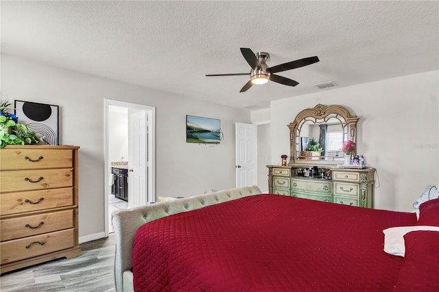 bedroom with a textured ceiling, light hardwood / wood-style floors, ceiling fan, and ensuite bath