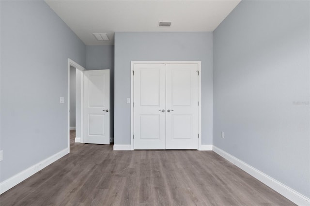 unfurnished bedroom with baseboards, a closet, visible vents, and wood finished floors