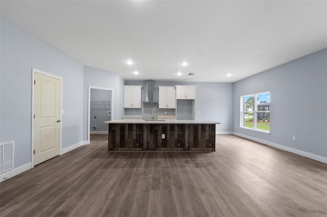 kitchen with hardwood / wood-style flooring, white cabinets, wall chimney range hood, and an island with sink