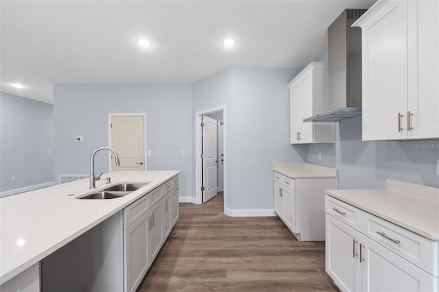 kitchen featuring dark wood-style floors, light countertops, wall chimney range hood, a sink, and recessed lighting