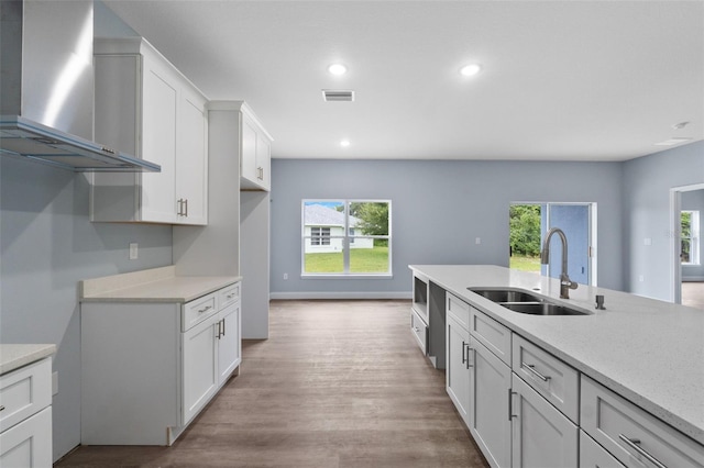 kitchen with sink, light wood-type flooring, light stone countertops, white cabinetry, and wall chimney range hood