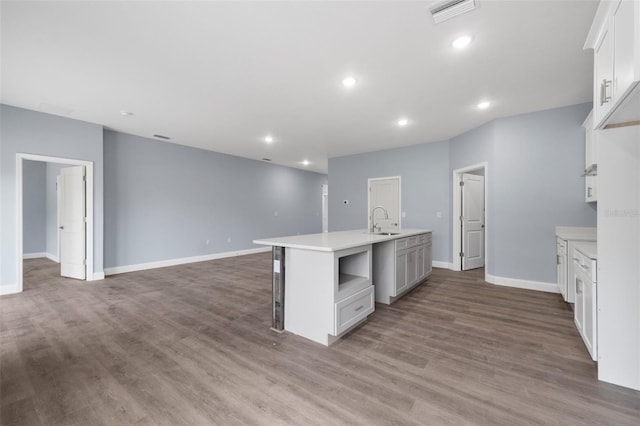 kitchen with visible vents, white cabinets, an island with sink, wood finished floors, and a sink