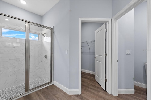 bathroom with a stall shower, baseboards, a walk in closet, and wood finished floors