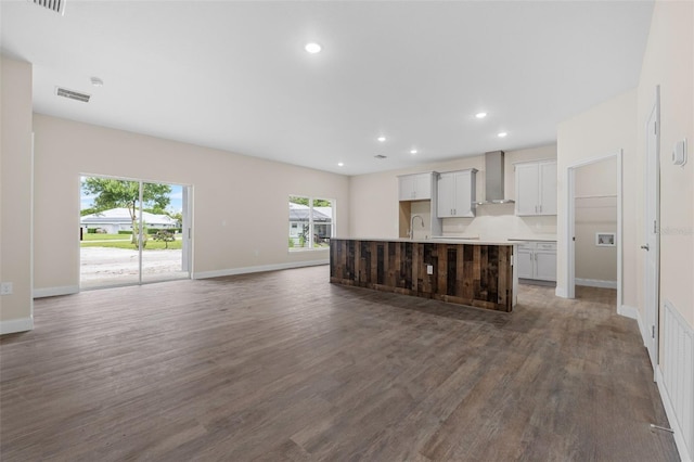 kitchen with wall chimney exhaust hood, a kitchen island with sink, sink, and dark hardwood / wood-style floors