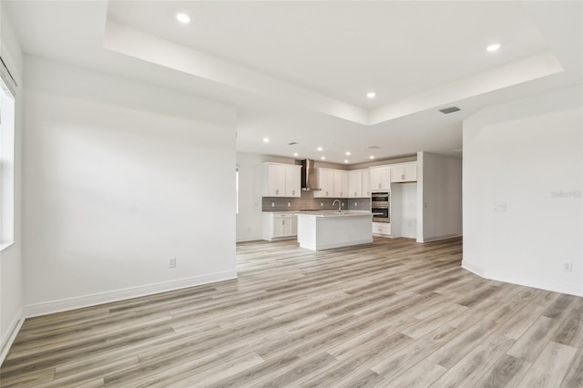 unfurnished living room featuring a raised ceiling, visible vents, light wood-style flooring, and baseboards