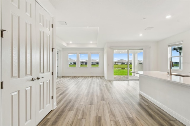 hall with baseboards, a raised ceiling, light wood-style floors, a sink, and recessed lighting