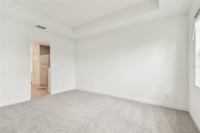 empty room with a tray ceiling, light carpet, visible vents, and baseboards