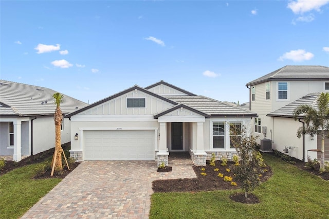 view of front of house with an attached garage, central air condition unit, stone siding, decorative driveway, and board and batten siding