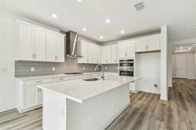 kitchen with gas cooktop, wall chimney exhaust hood, a sink, and white cabinets