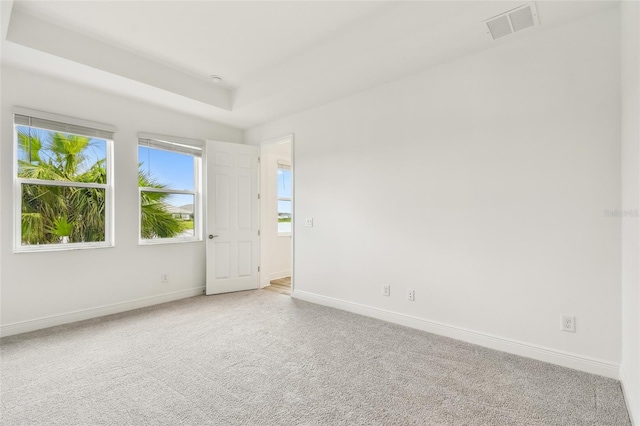 empty room with light carpet, baseboards, visible vents, and a raised ceiling