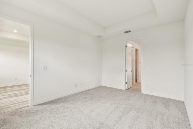 empty room with recessed lighting, a raised ceiling, light colored carpet, visible vents, and baseboards