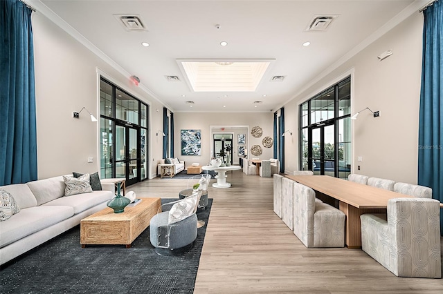 living room with light wood-type flooring, a skylight, crown molding, and french doors