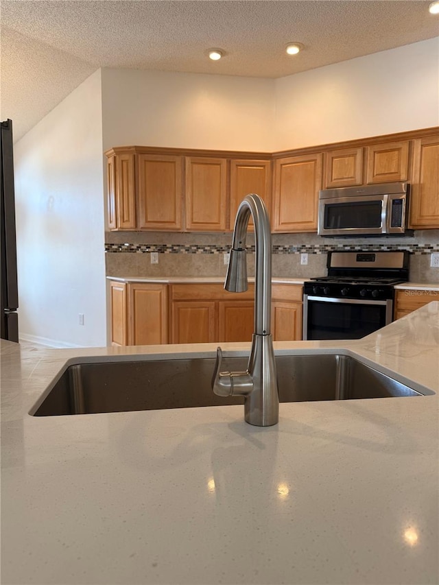 kitchen with light stone counters, a textured ceiling, appliances with stainless steel finishes, and tasteful backsplash