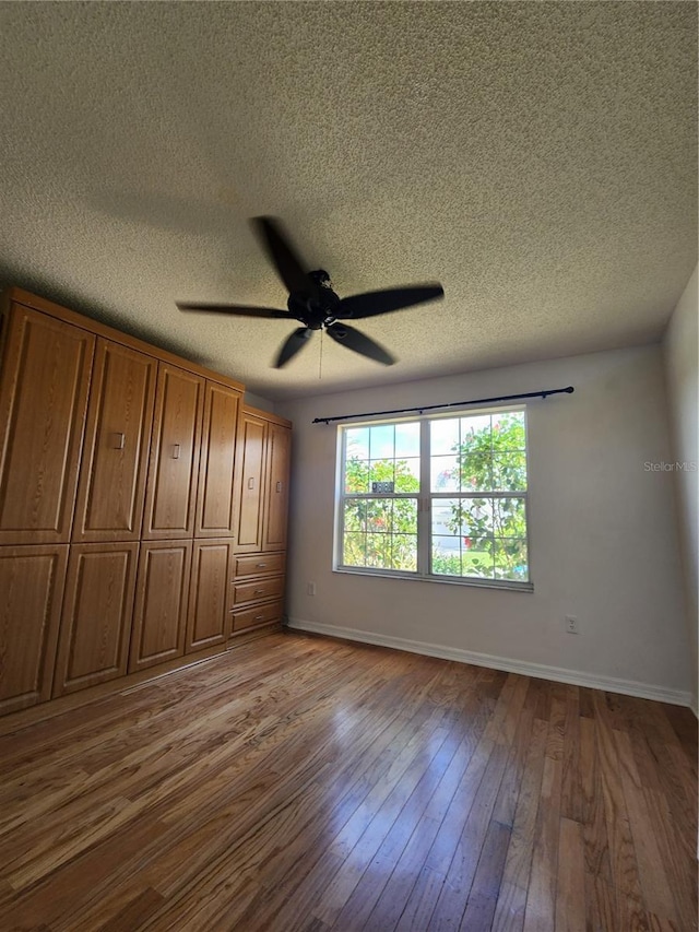 unfurnished bedroom featuring ceiling fan, a textured ceiling, and hardwood / wood-style flooring