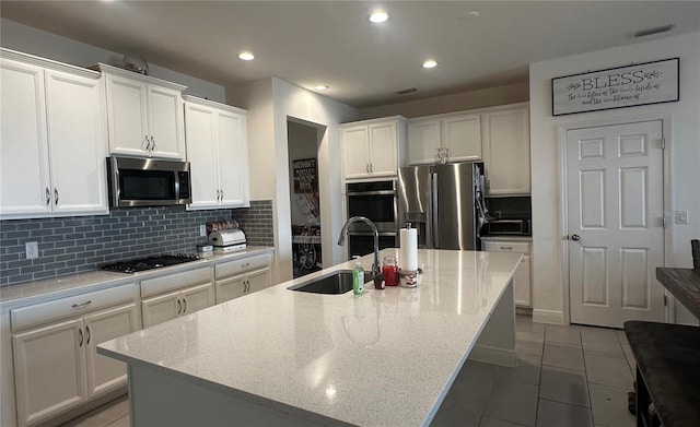 kitchen featuring sink, light stone countertops, an island with sink, appliances with stainless steel finishes, and white cabinetry