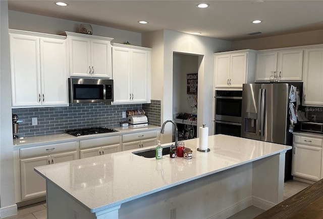 kitchen with stainless steel appliances, light stone counters, a kitchen island with sink, and sink