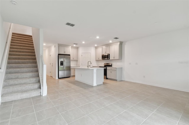 kitchen featuring appliances with stainless steel finishes, light tile patterned flooring, a kitchen island with sink, and sink