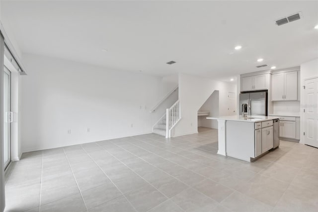 kitchen featuring stainless steel appliances, light tile patterned floors, a kitchen island with sink, and sink