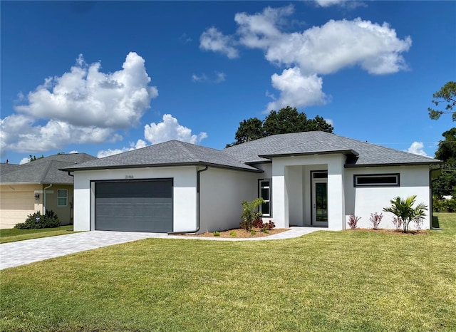 prairie-style home featuring stucco siding, roof with shingles, decorative driveway, a front yard, and a garage