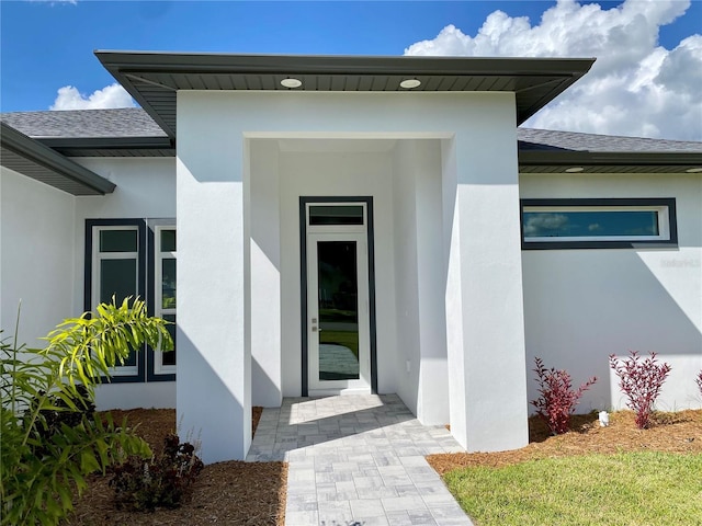entrance to property featuring stucco siding and roof with shingles