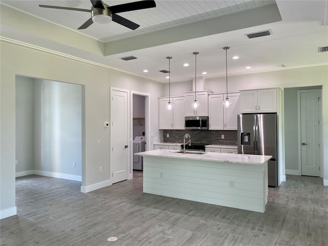 kitchen with light wood finished floors, a ceiling fan, appliances with stainless steel finishes, an island with sink, and backsplash