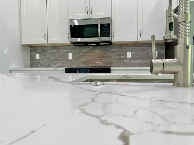 kitchen with decorative backsplash, white cabinets, stainless steel microwave, and light stone counters