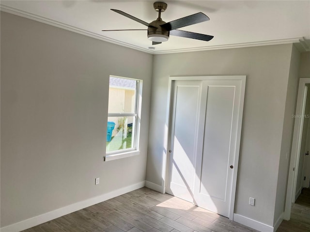 unfurnished bedroom featuring a closet, crown molding, baseboards, wood finished floors, and a ceiling fan