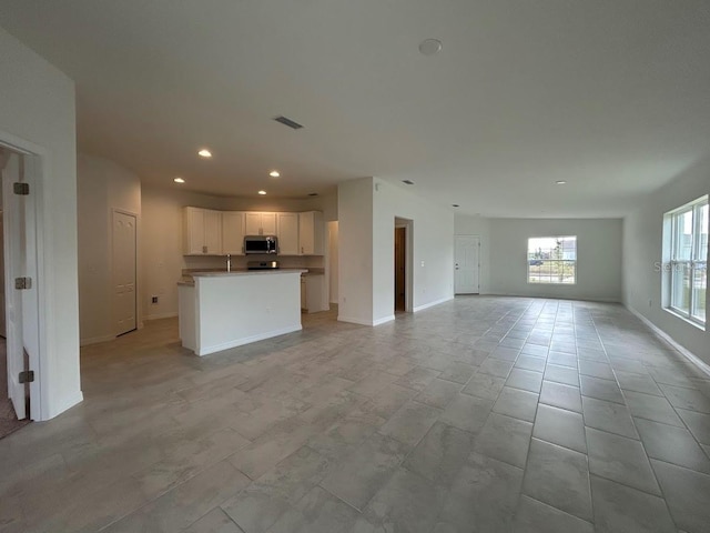 unfurnished living room with recessed lighting, a sink, visible vents, and baseboards