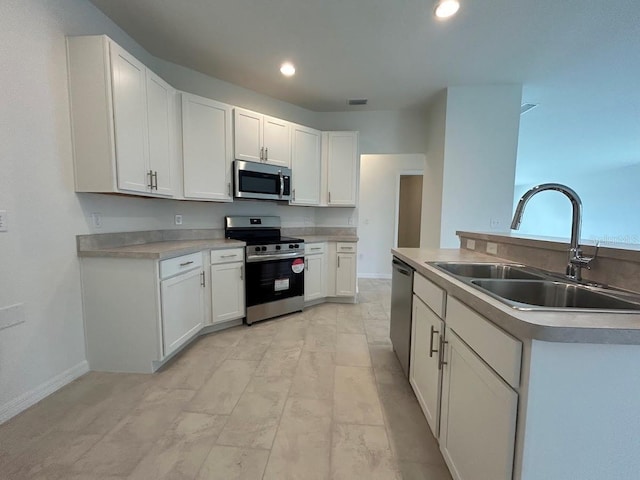 kitchen with baseboards, stainless steel appliances, light countertops, white cabinetry, and a sink