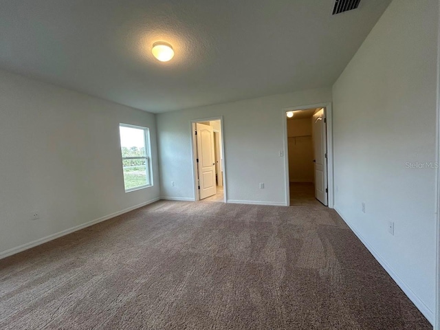 unfurnished bedroom featuring visible vents, light carpet, a spacious closet, and baseboards