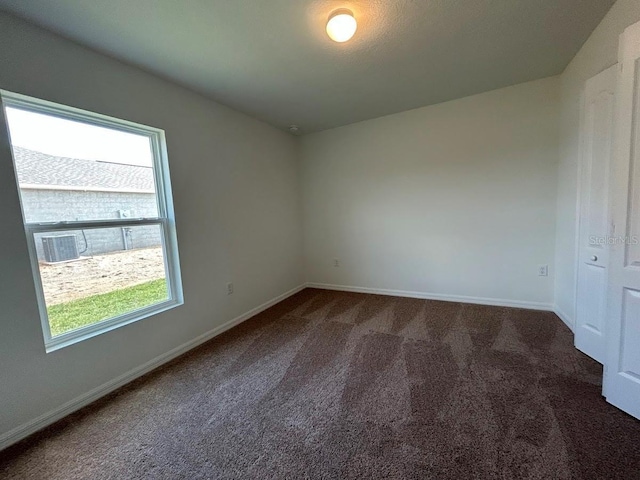 empty room with baseboards, dark colored carpet, and a healthy amount of sunlight