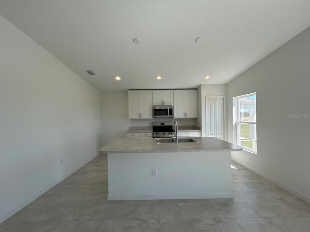 kitchen with light countertops, stainless steel appliances, a center island with sink, white cabinetry, and a sink