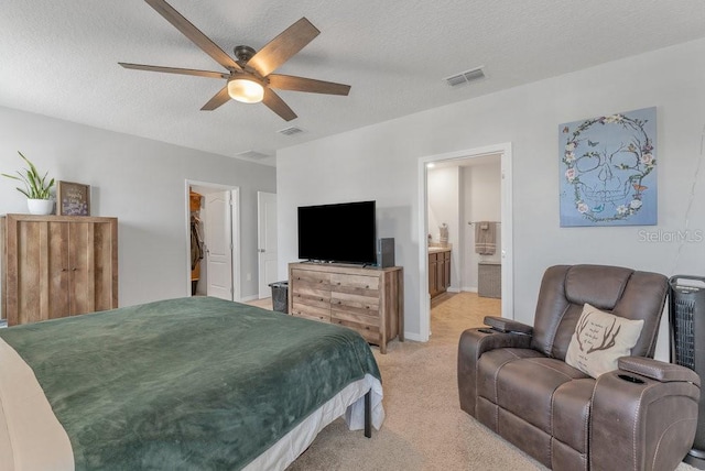 bedroom with a textured ceiling, light carpet, ensuite bathroom, a spacious closet, and ceiling fan