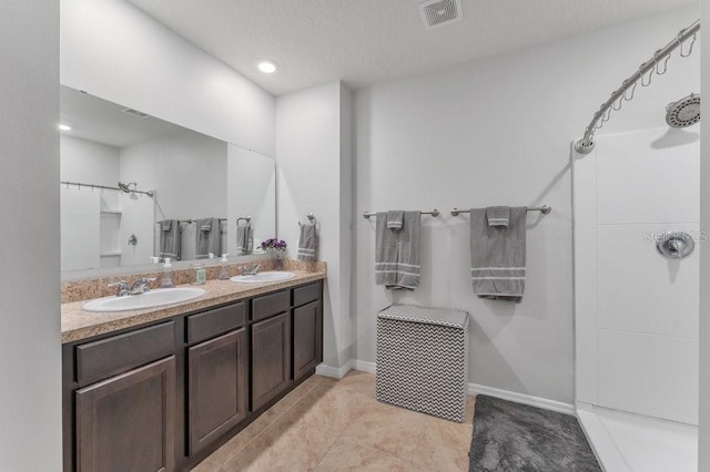 bathroom with a textured ceiling, a shower, tile patterned flooring, and vanity