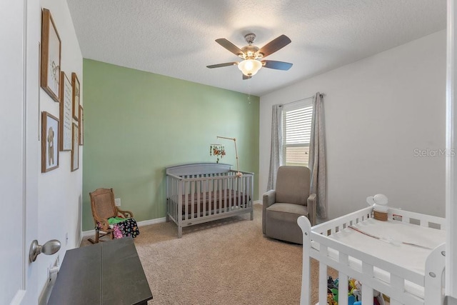 bedroom with light colored carpet, ceiling fan, a crib, and a textured ceiling