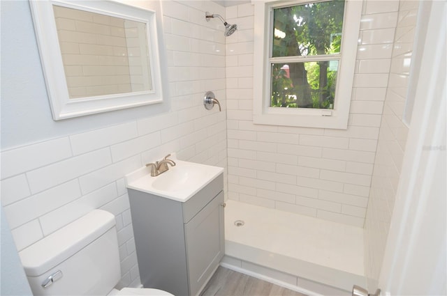 bathroom with tile walls, tiled shower, vanity, hardwood / wood-style flooring, and toilet