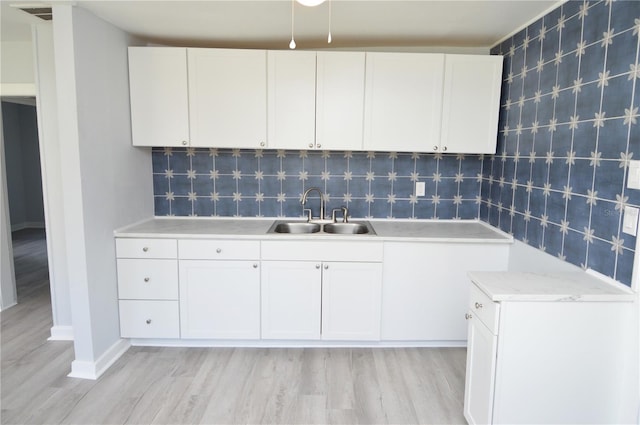 kitchen featuring decorative backsplash, light wood-type flooring, white cabinetry, and sink