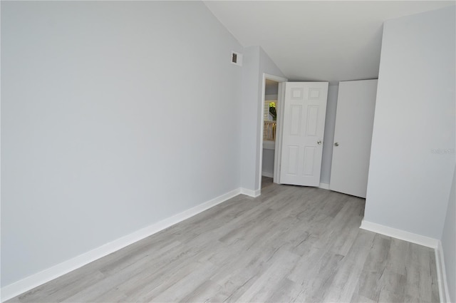 empty room with light hardwood / wood-style floors and vaulted ceiling