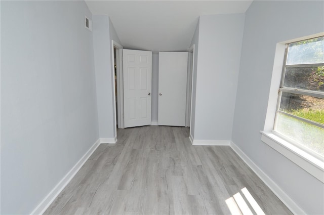 unfurnished bedroom featuring light hardwood / wood-style floors, multiple windows, and vaulted ceiling