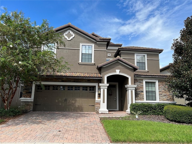 mediterranean / spanish-style home featuring a tiled roof, an attached garage, stone siding, and decorative driveway