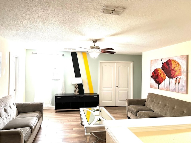 living area featuring visible vents, a textured ceiling, a ceiling fan, and wood finished floors