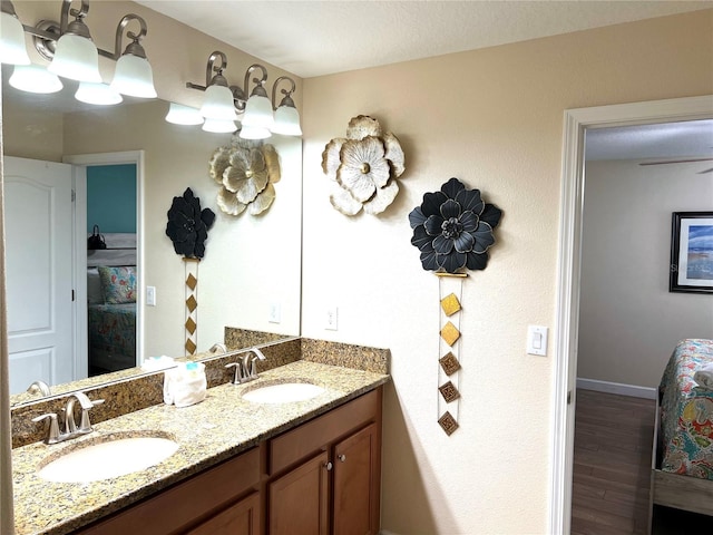full bathroom with double vanity, baseboards, a sink, and wood finished floors