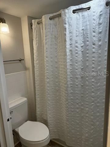 bathroom featuring curtained shower, tile walls, and toilet