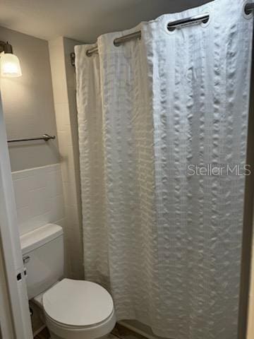 full bathroom with toilet and a shower with shower curtain