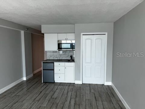 kitchen with dark countertops, a textured ceiling, white cabinets, dark wood finished floors, and baseboards