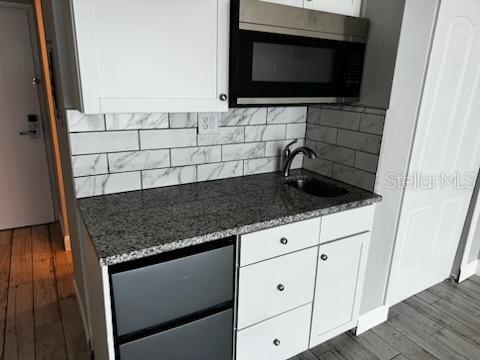 kitchen with white cabinets, a sink, dark stone countertops, stainless steel microwave, and dark wood-style flooring