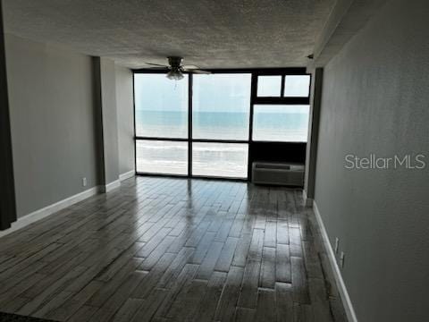 empty room featuring a wall of windows, a water view, ceiling fan, dark hardwood / wood-style floors, and a baseboard heating unit